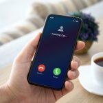 male hands holding phone with incoming call on the screen over a table in the room