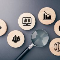 A flat lay of magnifying glass and wooden icons representing data analysis, audience targeting, performance metrics, and social media goals for effective content strategy See Less